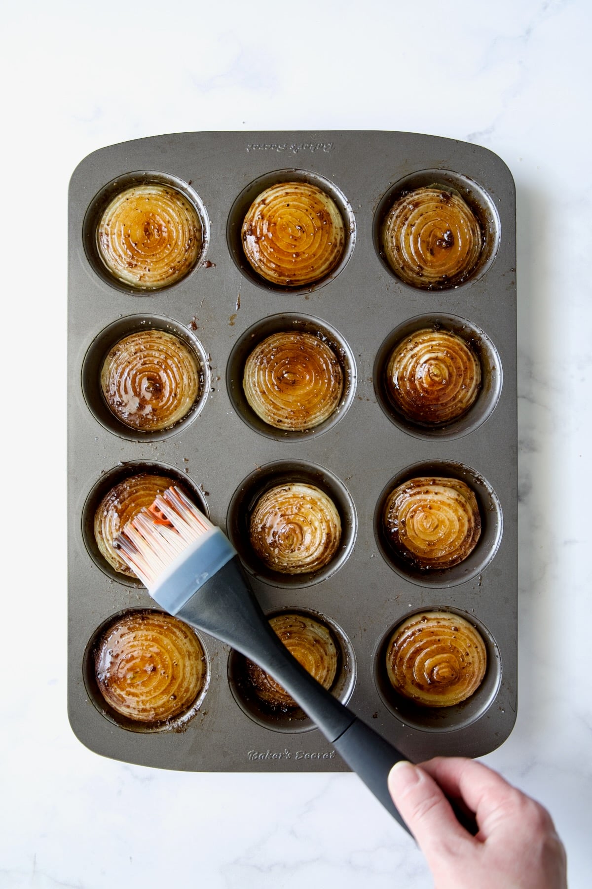 Onions halves in nonstick muffin pan topped with ghee and beef base with pastry brush smoothing it out..