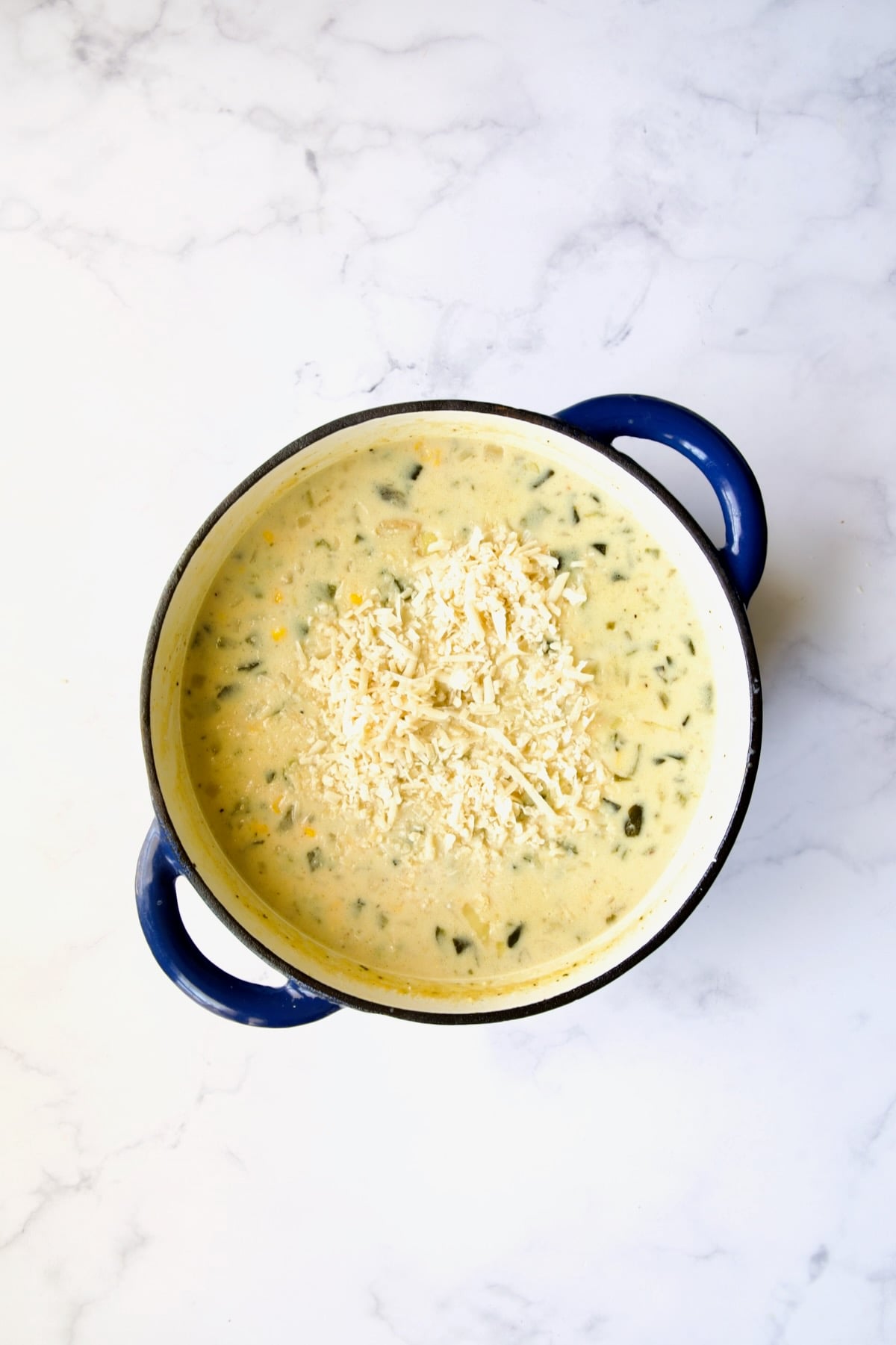 Cheese being added to soup in blue Dutch oven.