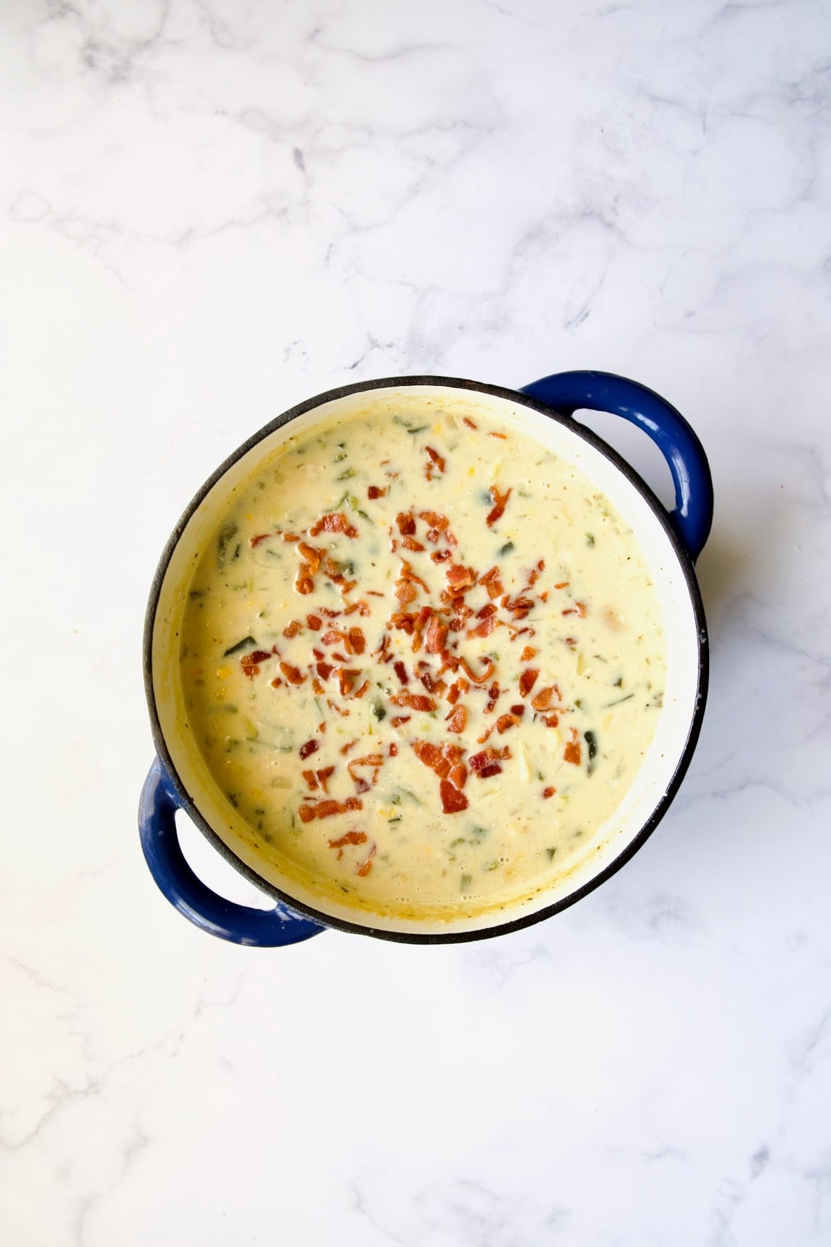 Bacon added to soup in blue Dutch oven.