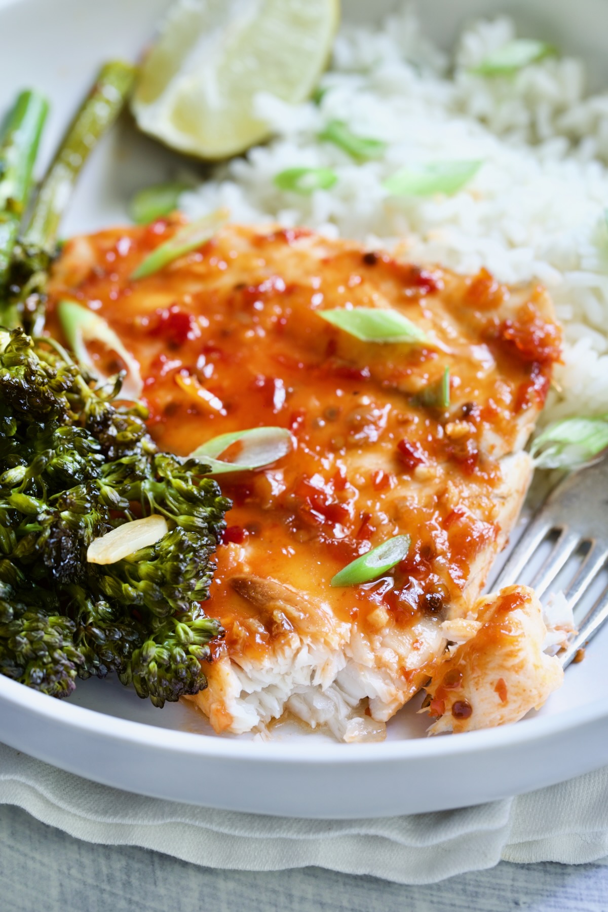 Sheet Pan Thai Baked Fish with Broccolini on white plate with fork garnished with scallions.