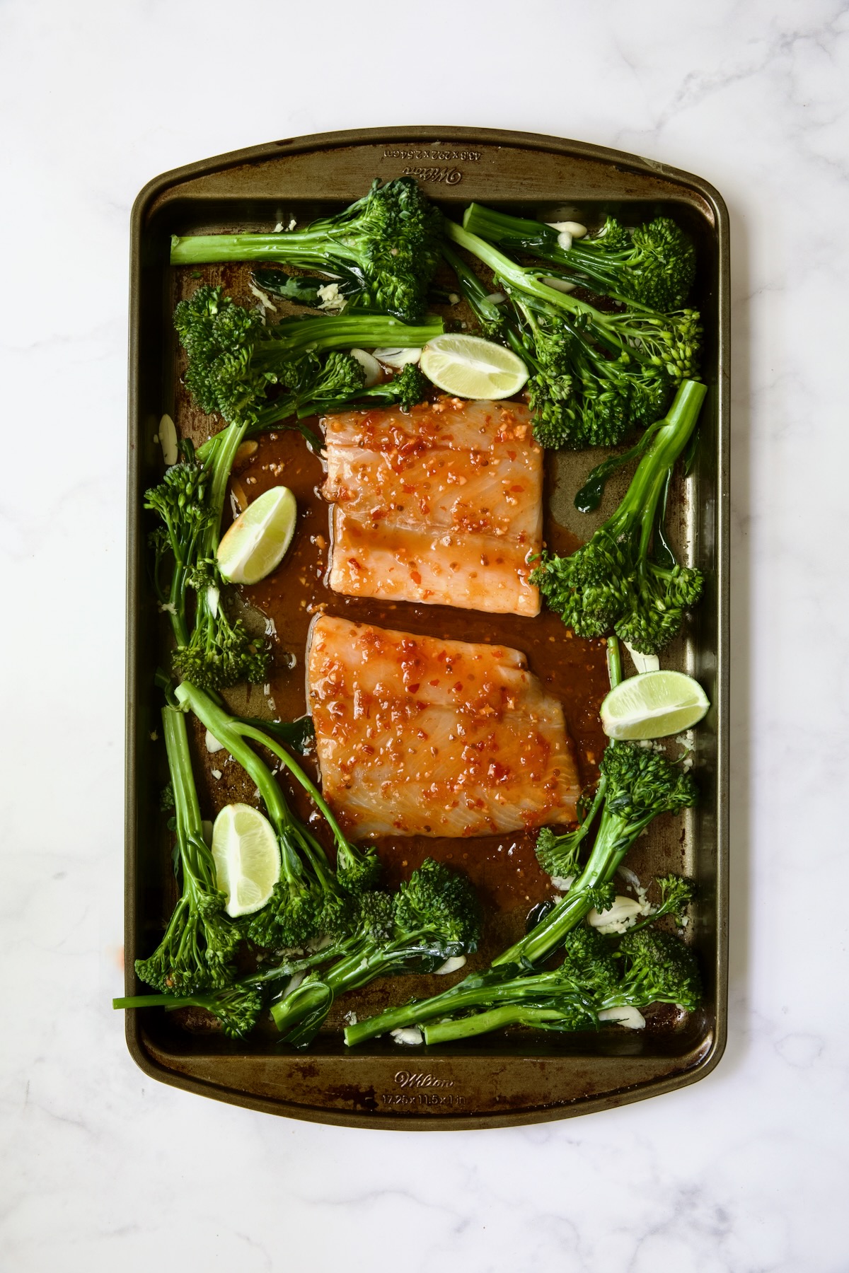 Broccolini and two pieces of fish with glaze poured over on rimmed sheet pan.