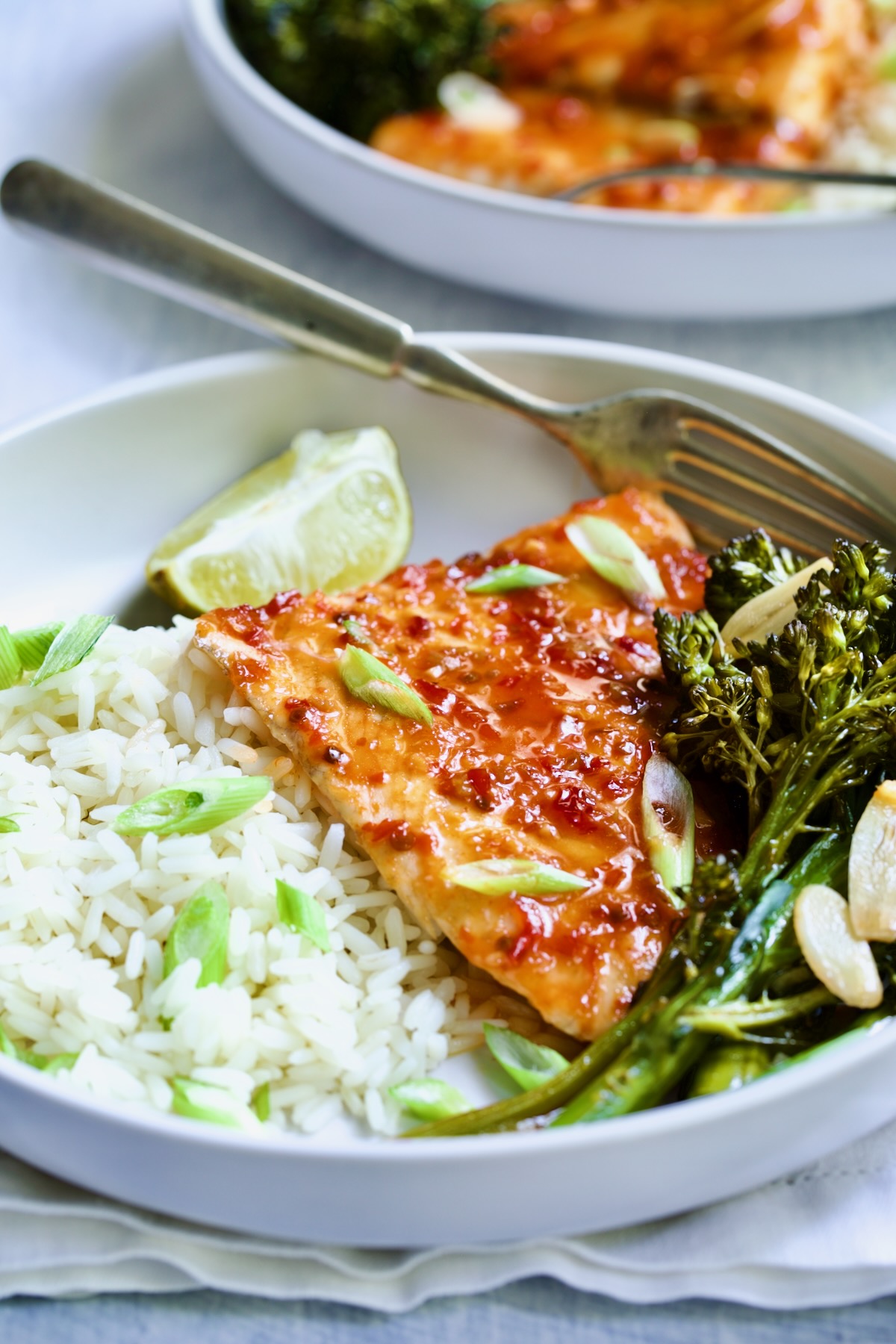 Sheet Pan Thai Baked Fish with Broccolini on white plate with fork and lime wedge.