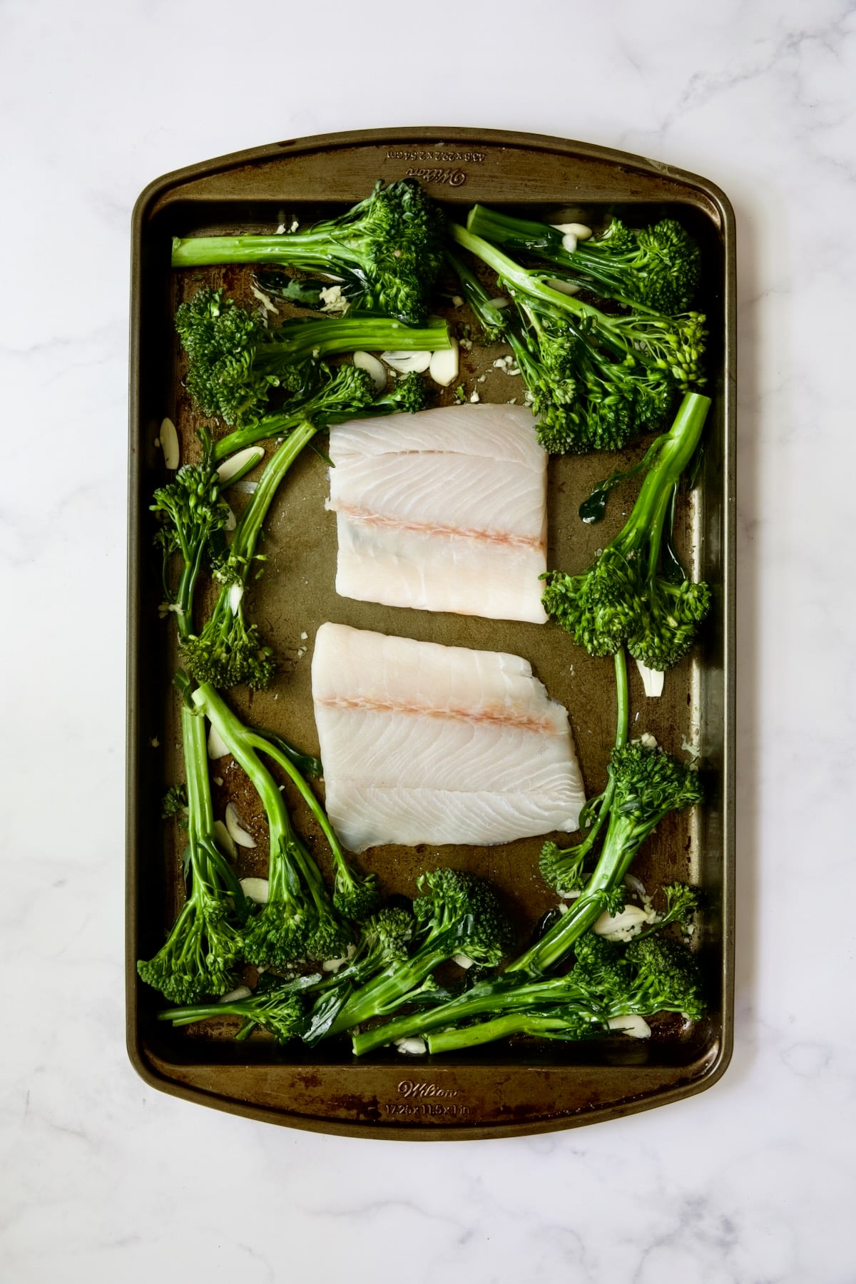 Broccolini and two pieces of fish on rimmed sheet pan.
