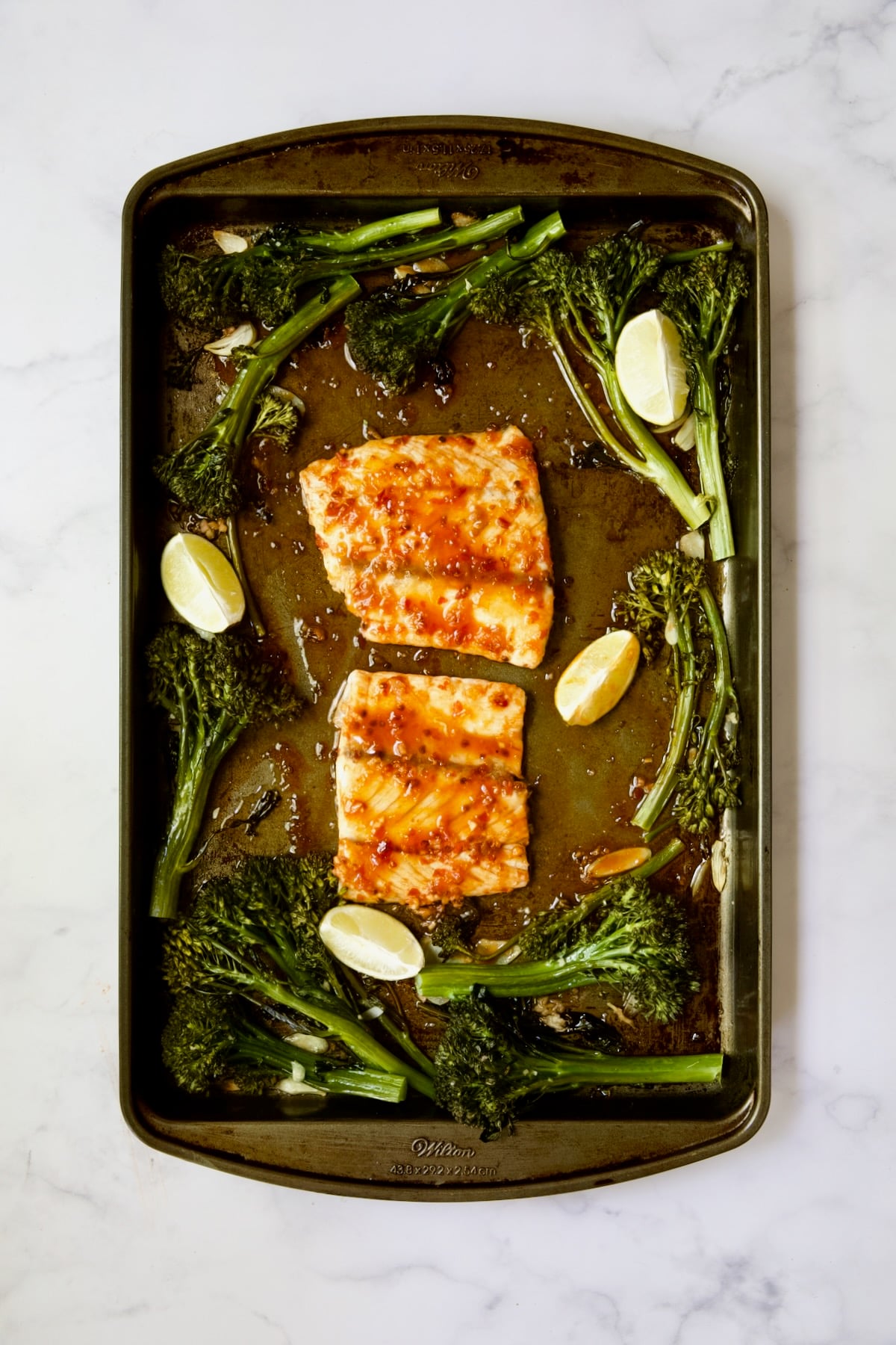 Broccolini and two pieces of fish on rimmed sheet pan after being baked.