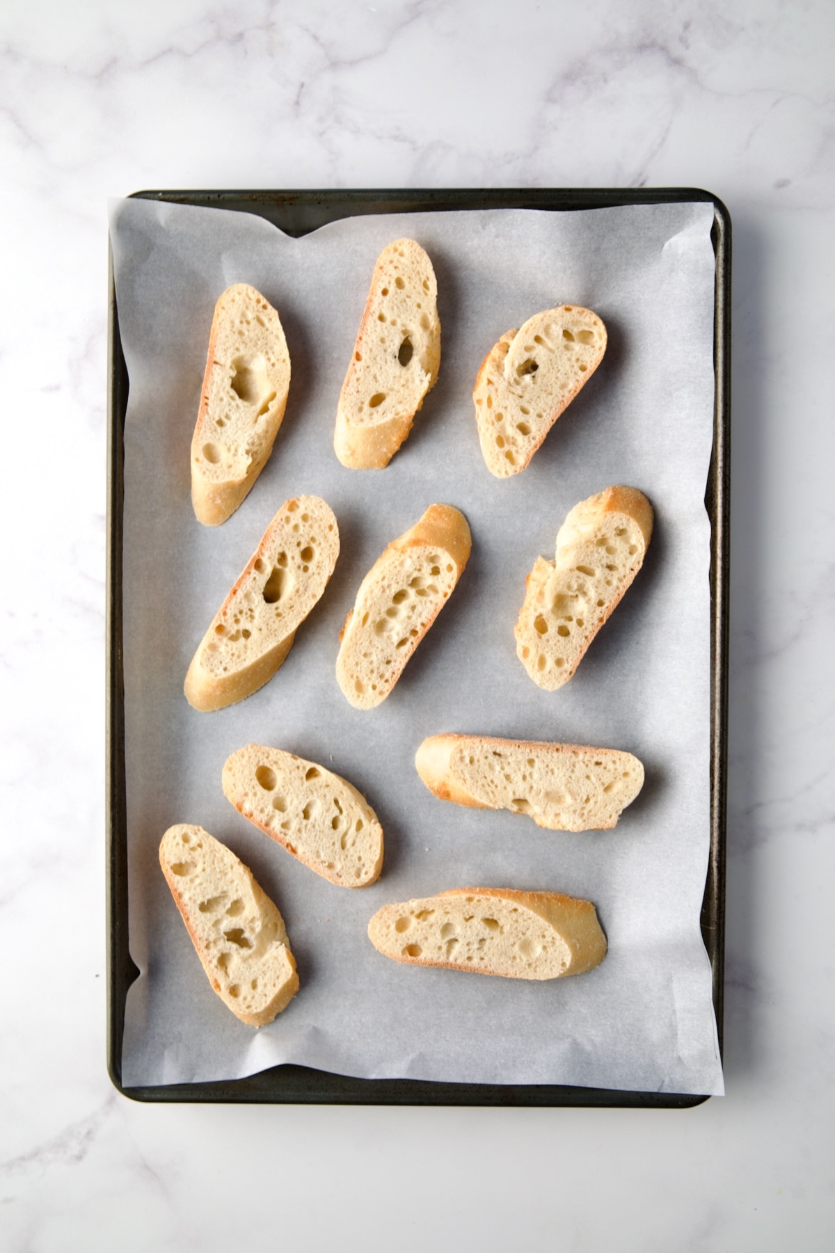 Bread slices on parchment paper lined rimmed baking sheet.