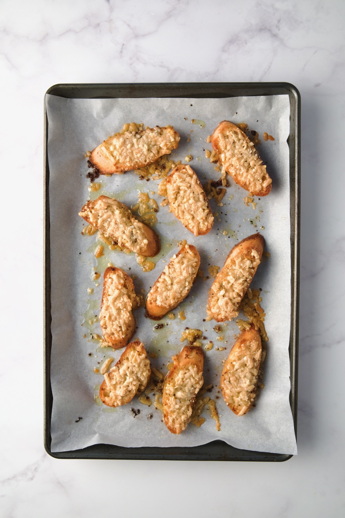 Toasted parmesan toasts on parchment paper lined rimmed baking sheet.