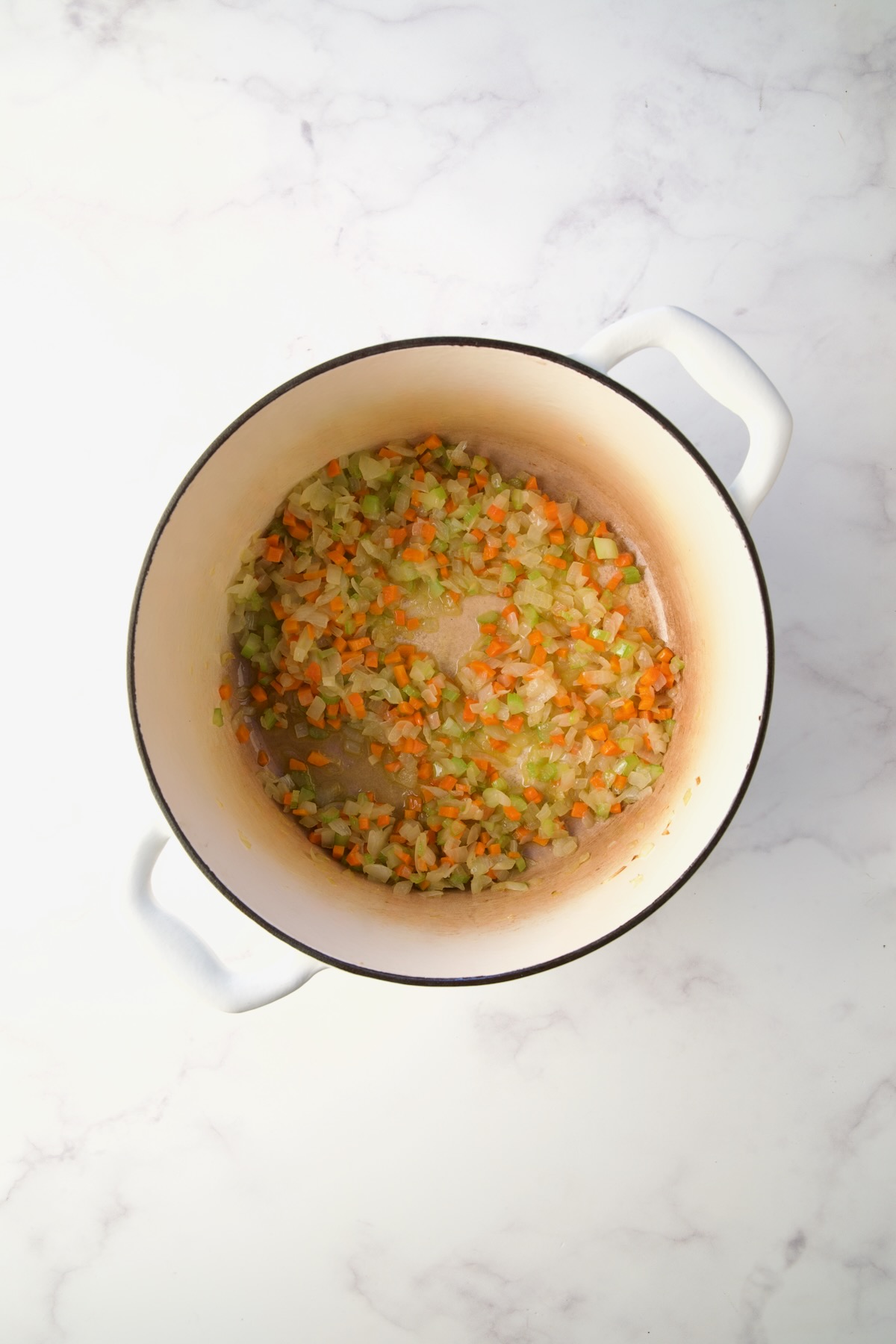 Cooked onions, carrot and celery in white Dutch oven.
