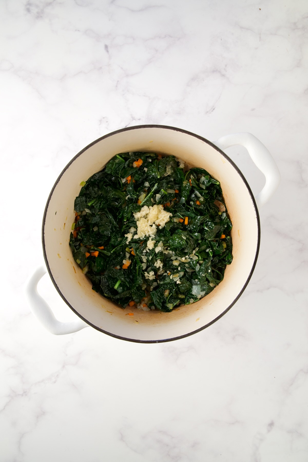 Cooked onions, carrots, celery, kale and garlic in white Dutch oven.