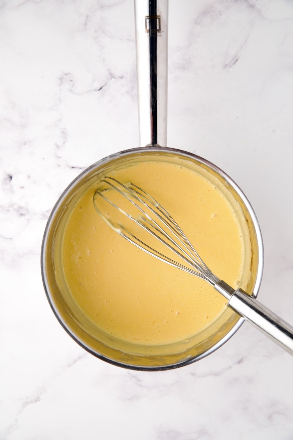 Cheese sauce with wire whisk in stainless steel saucepan.
