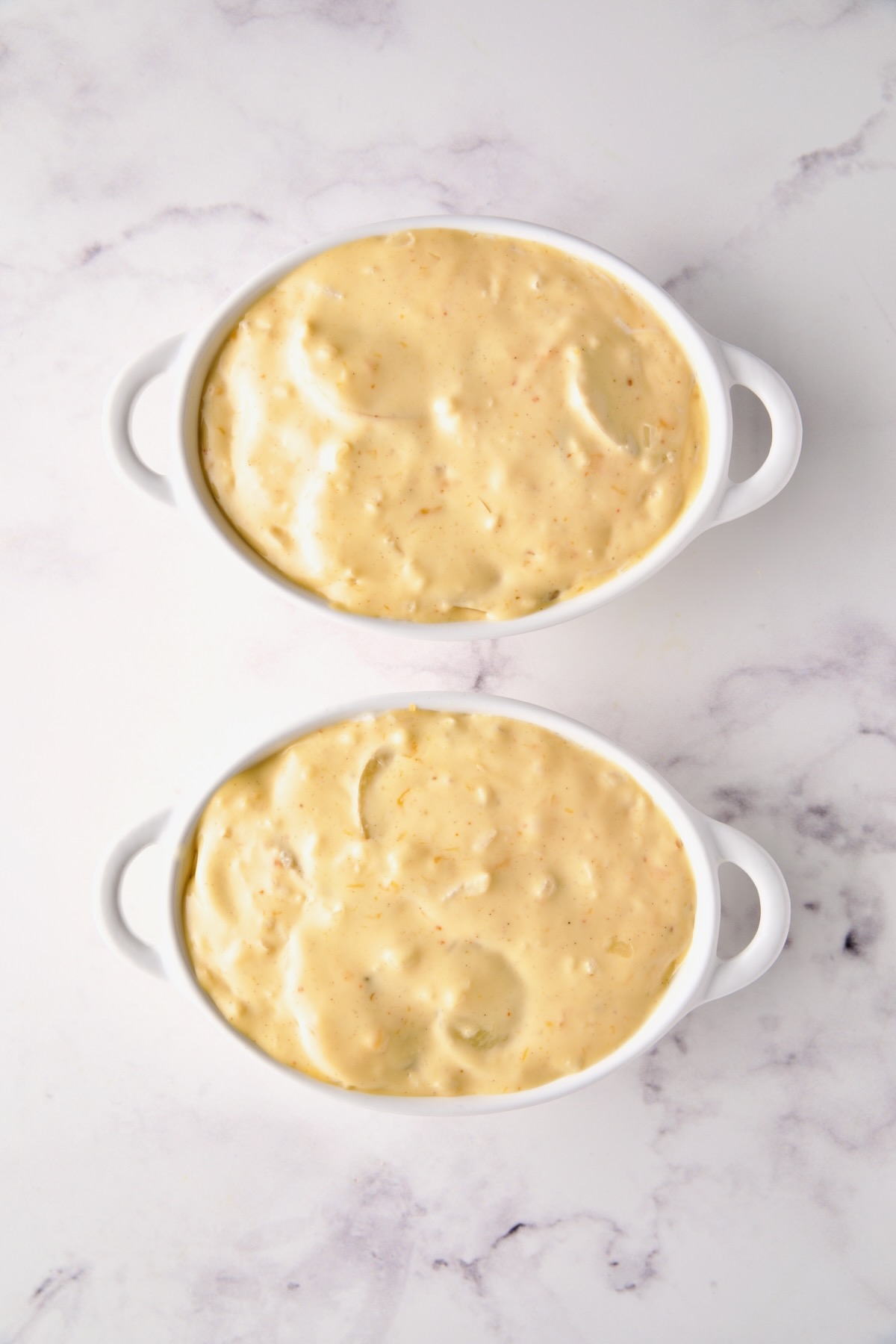 Fully assembled au gratin potatoes in white oval dishes ready to be baked.