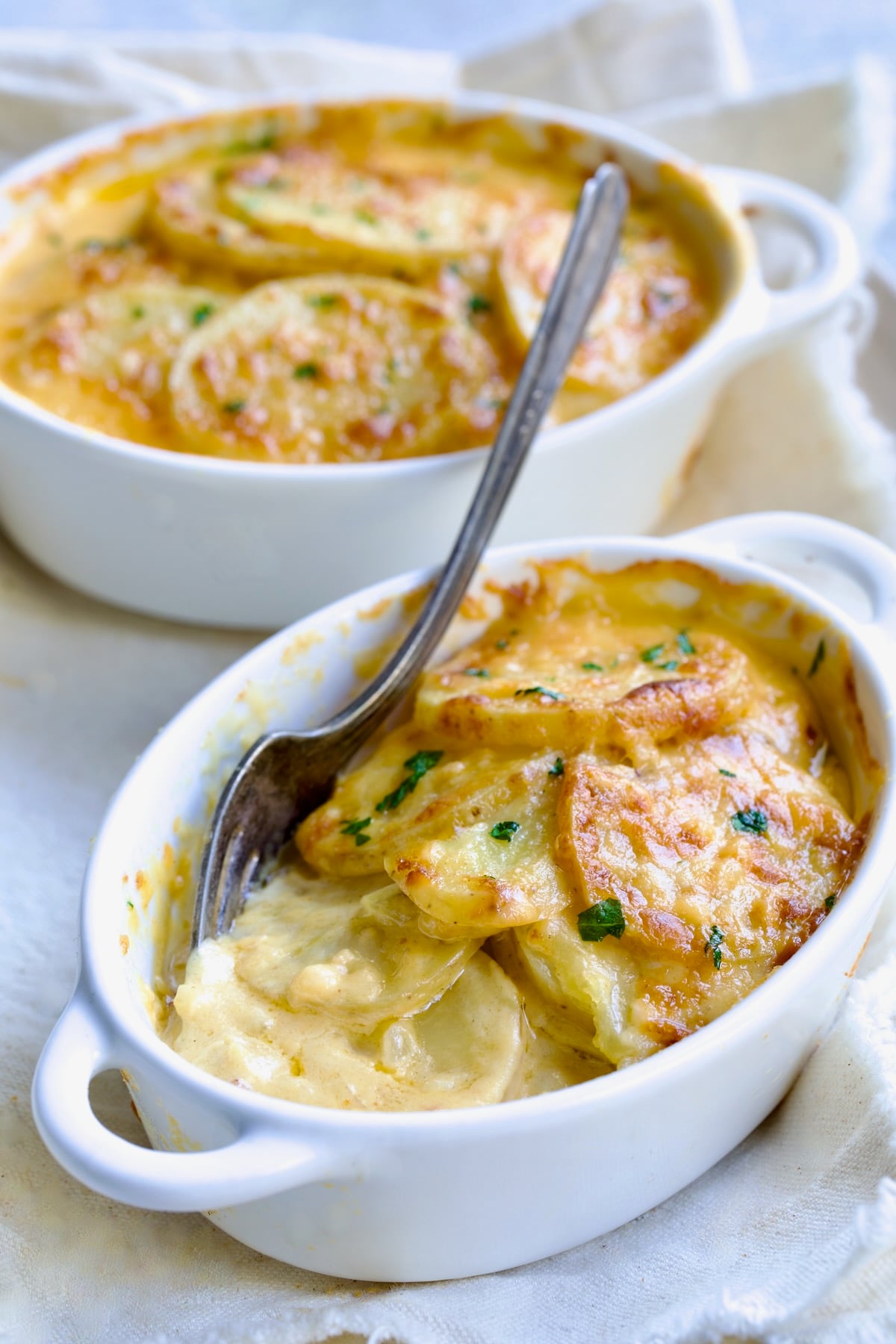 Two oval dishes of Au Gratin Potatoes for Two with fork digging into one.