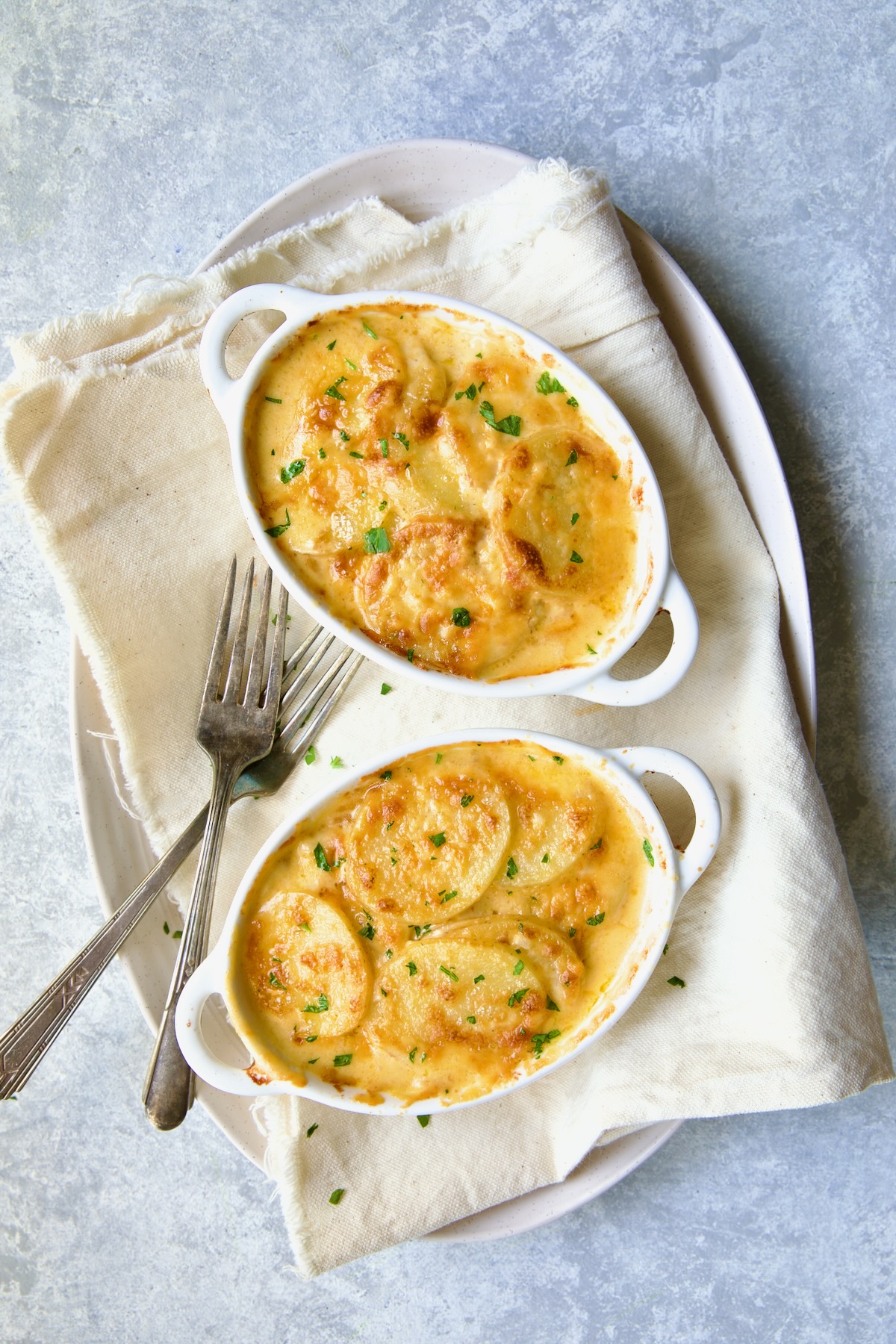 Two oval dishes of Au Gratin Potatoes for Two with two forks on white oval platter.