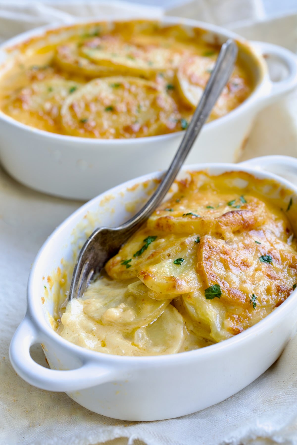 Two white oval dishes of Au Gratin Potatoes for Two with fork digging into one.
