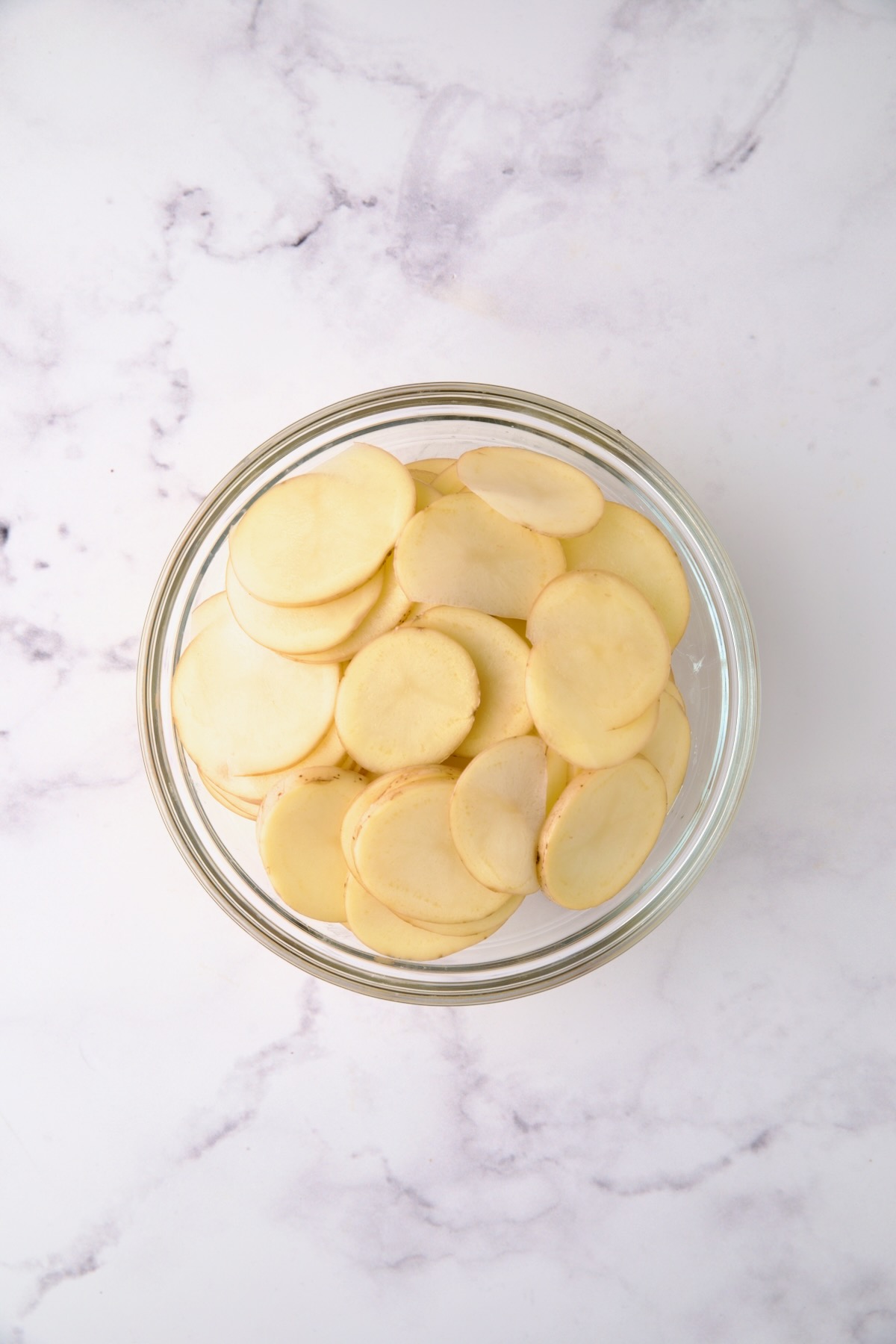 Thinly sliced Yukon Gold potatoes in glass bowl.