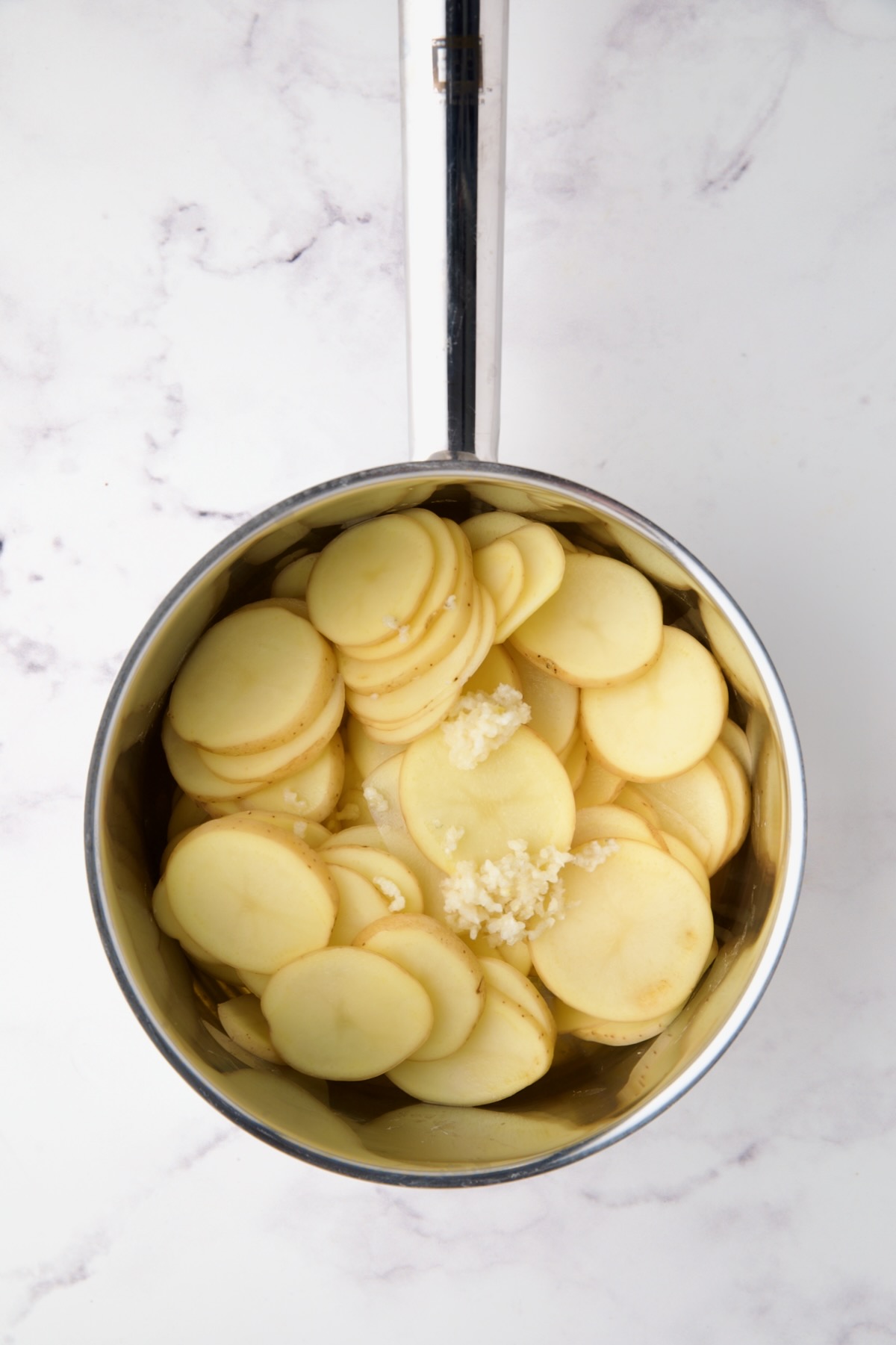 Thinly sliced Yukon Gold potatoes in stainless steel saucepan with onion and garlic.