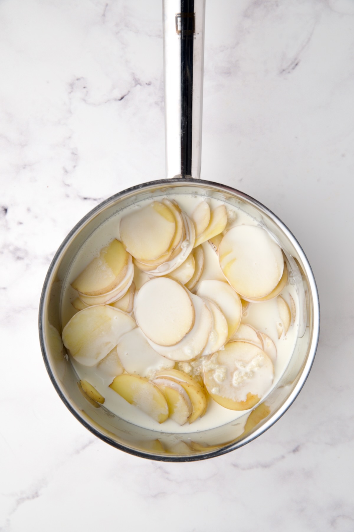 Cream added to potatoes in stainless steel saucepan.
