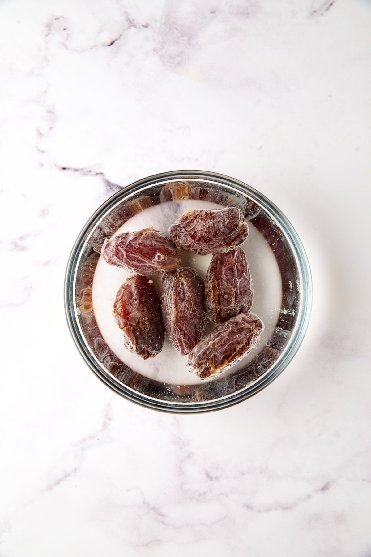 Six Medjool dates soaking in water in glass bowl.