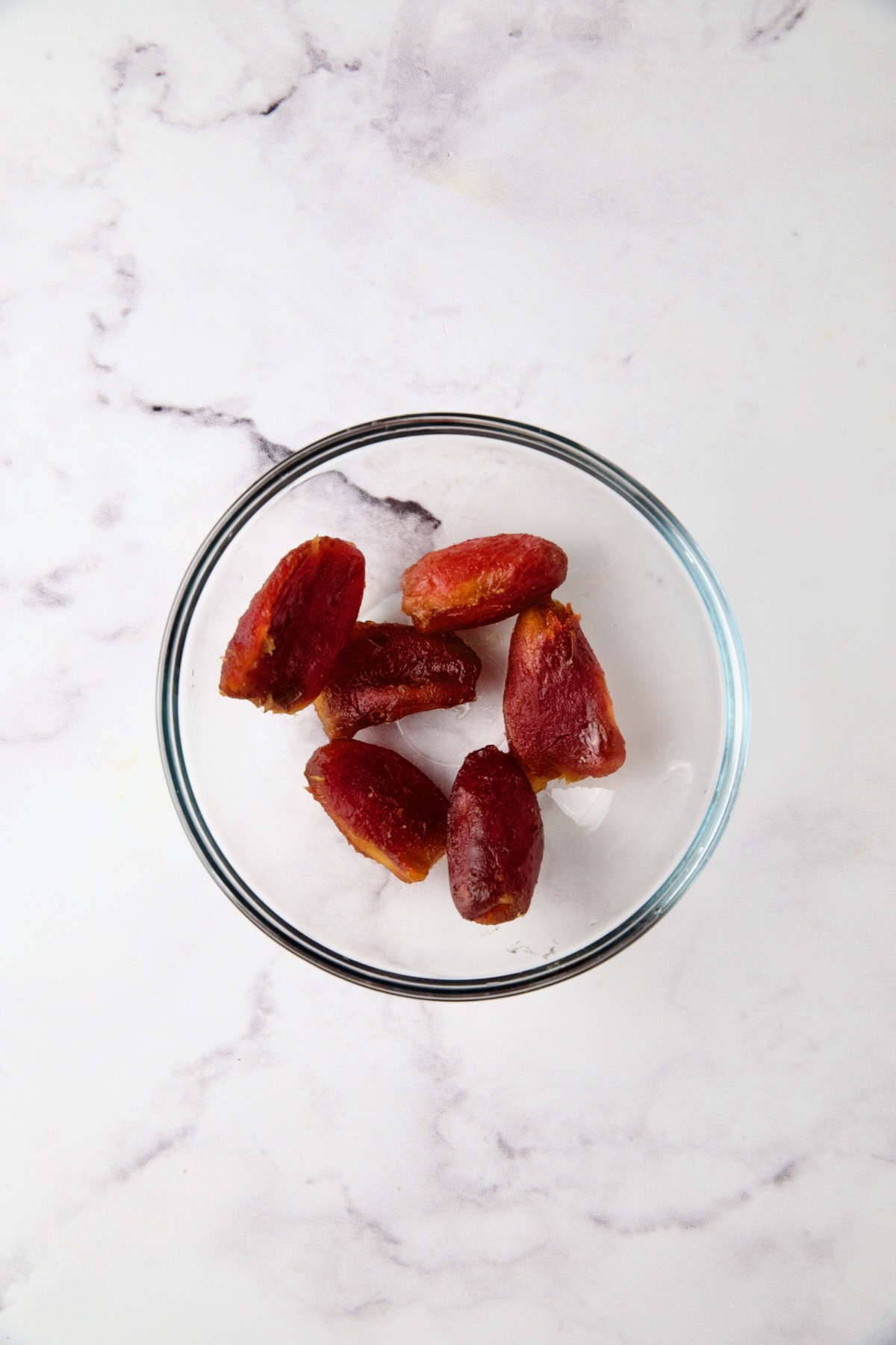 Six peeled Medjool dates in glass bowl.
