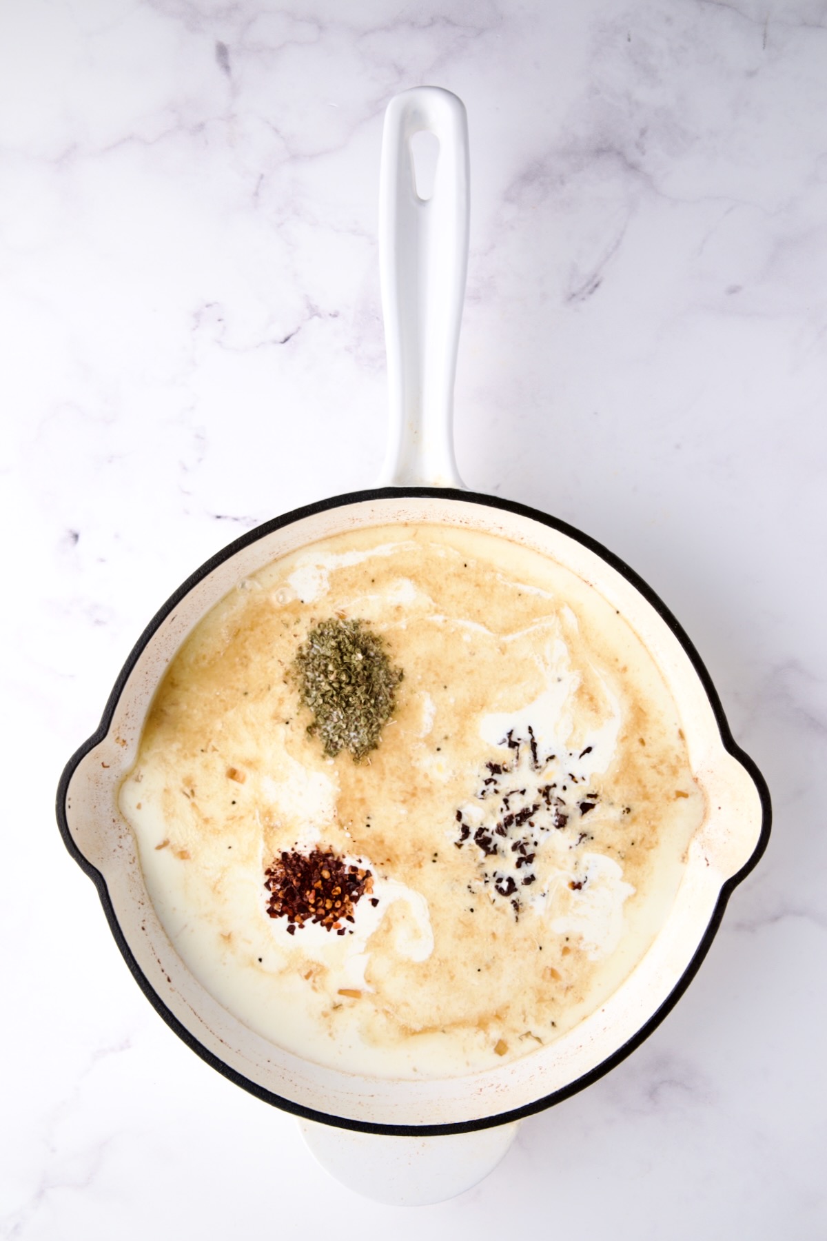 Chicken broth, heavy cream, sun dried tomatoes, dried oregano and red pepper flakes in white enamel cast iron skillet.