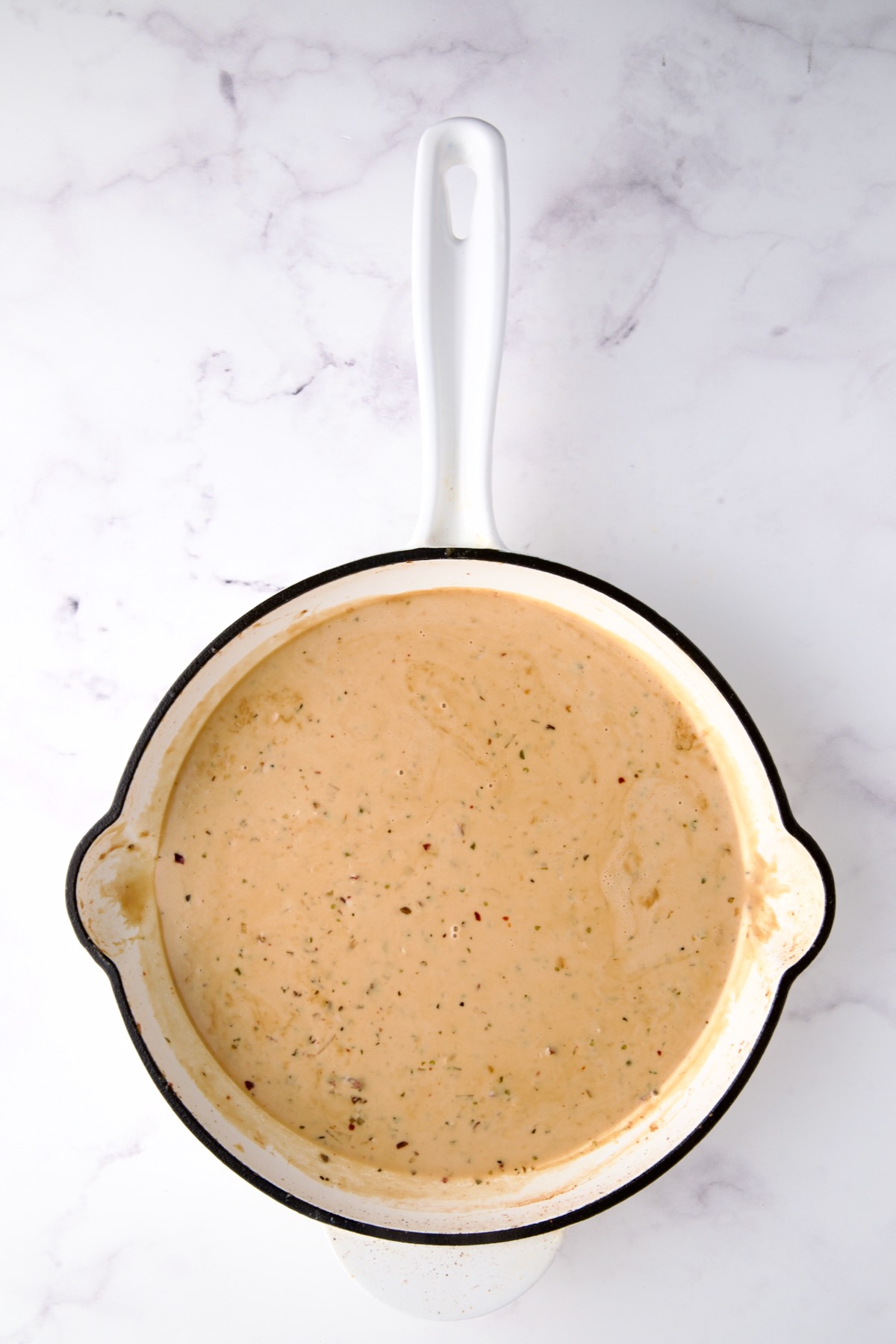 Finished cream sauce in white enamel cast iron skillet.