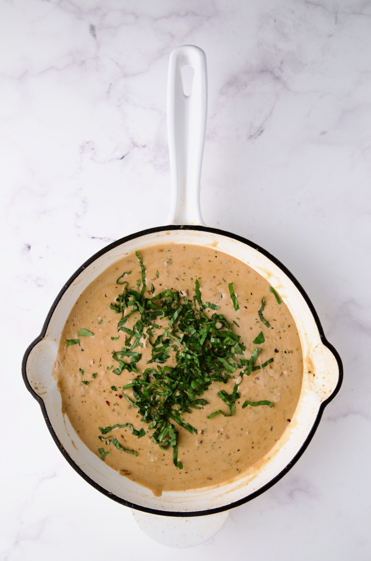 Finished sauce in white enamel cast iron skillet with fresh basil added.