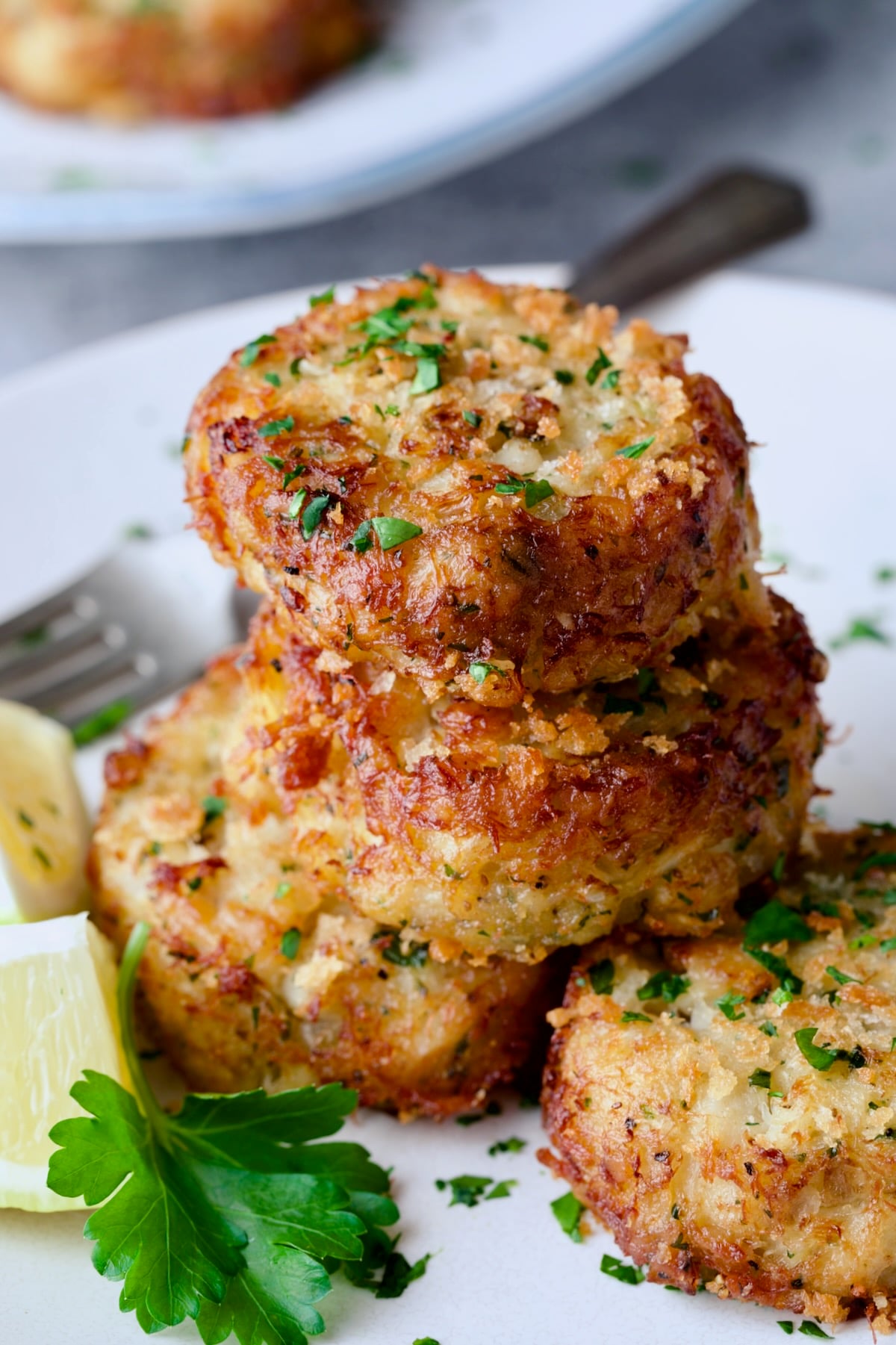 Stack of three Maryland-Style Crab Cakes on white plate garnished with parsley and lemon wedges.