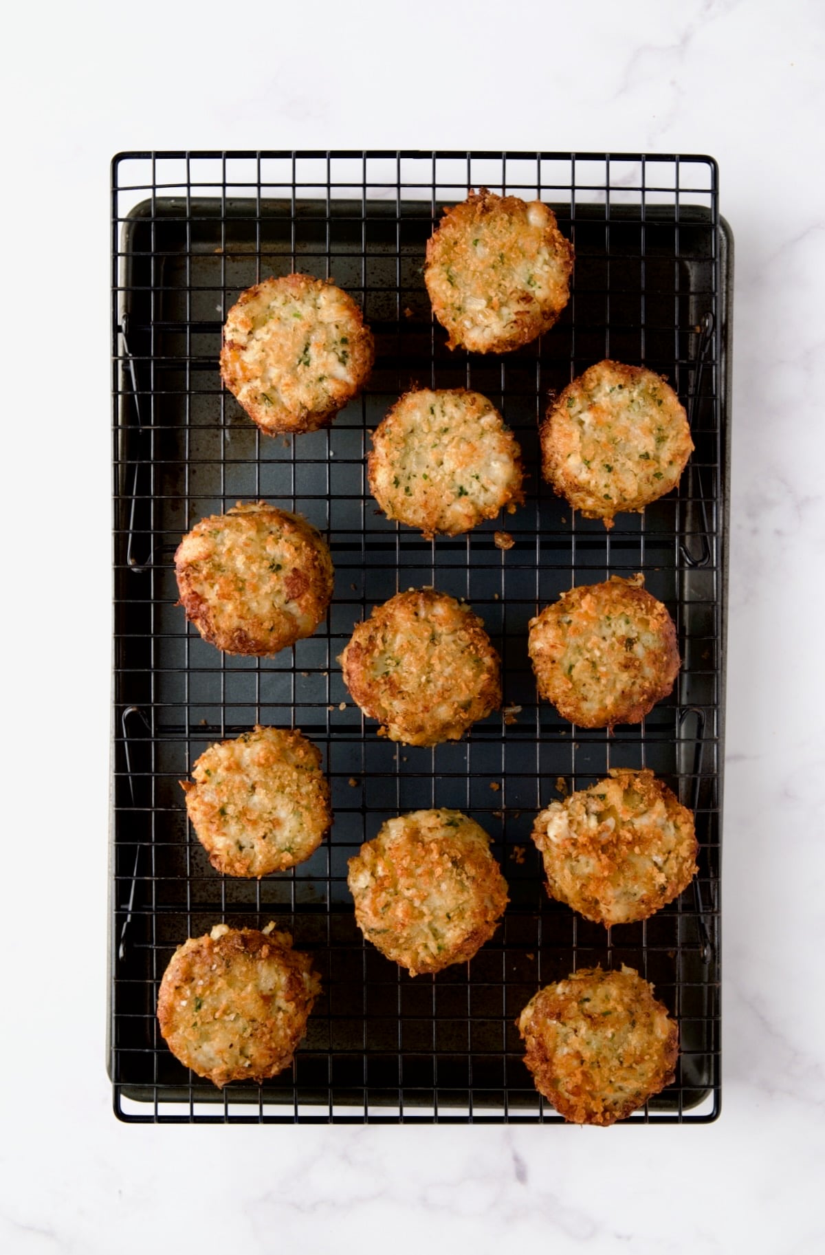 12 cooked crab cakes on cooling rack set over rimmed baking sheet.
