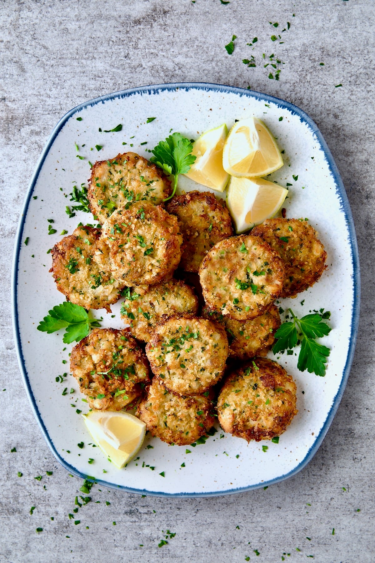 Maryland-Style Crab Cakes on blue-trimmed platter garnished with parsley, parsley sprigs and lemon wedges.