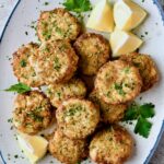 Maryland-Style Crab Cakes on blue-rimmed platter garnished with chopped fresh parsley, parsley sprigs and lemon wedges.
