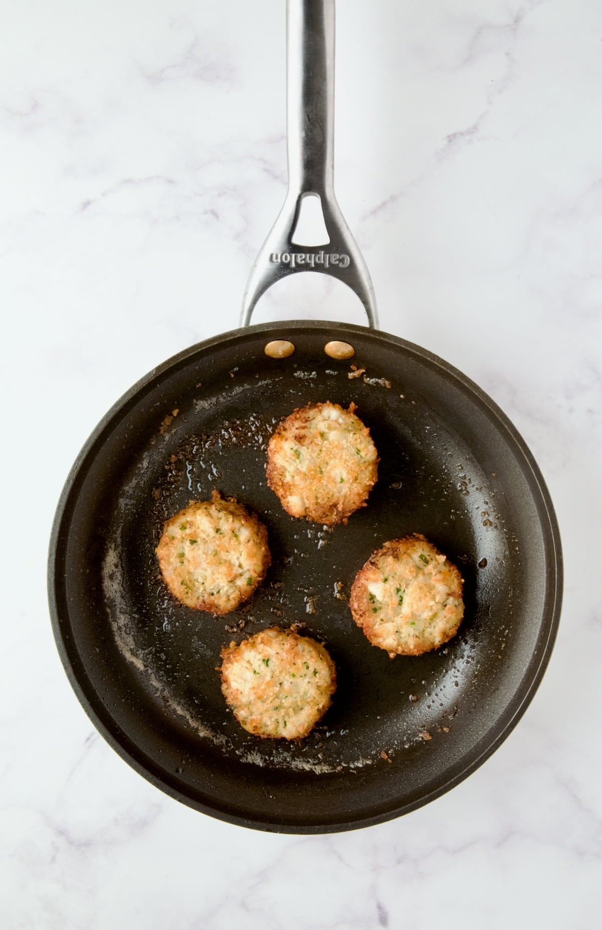Four browned crab cakes in nonstick skillet.