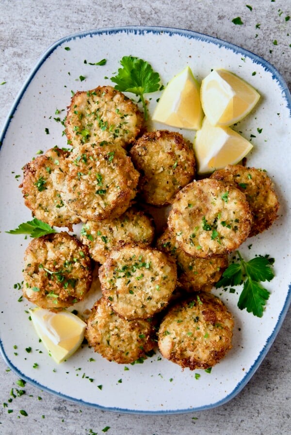Maryland-Style Crab Cakes on blue-rimmed platter garnished with chopped fresh parsley, parsley sprigs and lemon wedges.