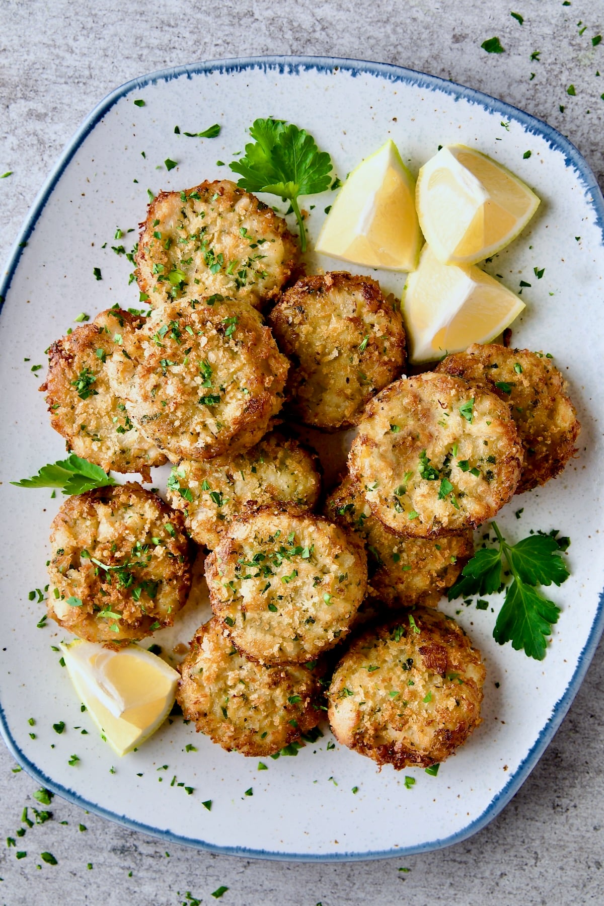 Maryland-Style Crab Cakes on blue-rimmed platter garnished with chopped fresh parsley, parsley sprigs and lemon wedges.