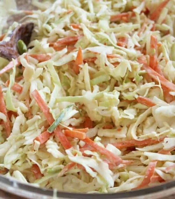 Coleslaw being mixed with serving utensils.