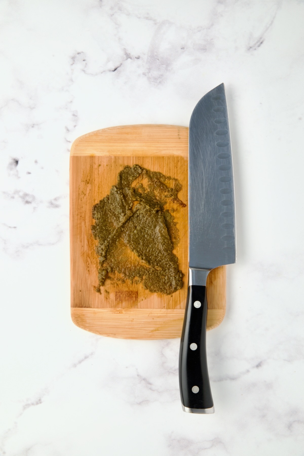 Mashed chipotle chiles on wood cutting board with chef knife.