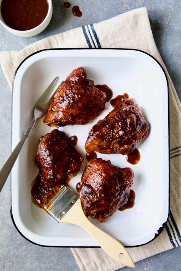 Four Baked BBQ Chicken Thighs in white enamel serving dish.