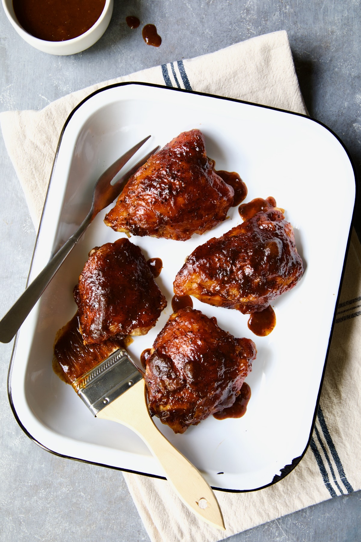 Four Baked BBQ Chicken Thighs in white enamel serving dish.