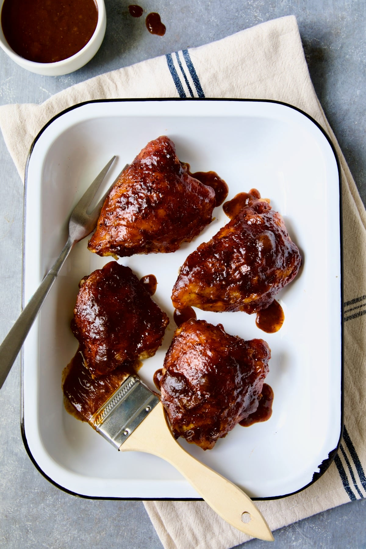 Four Baked BBQ Chicken Thighs in white enamel serving dish.