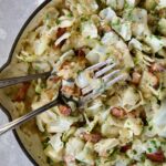 Two serving utensils serving up Fried Cabbage with Bacon from white enamel cast iron skillet.