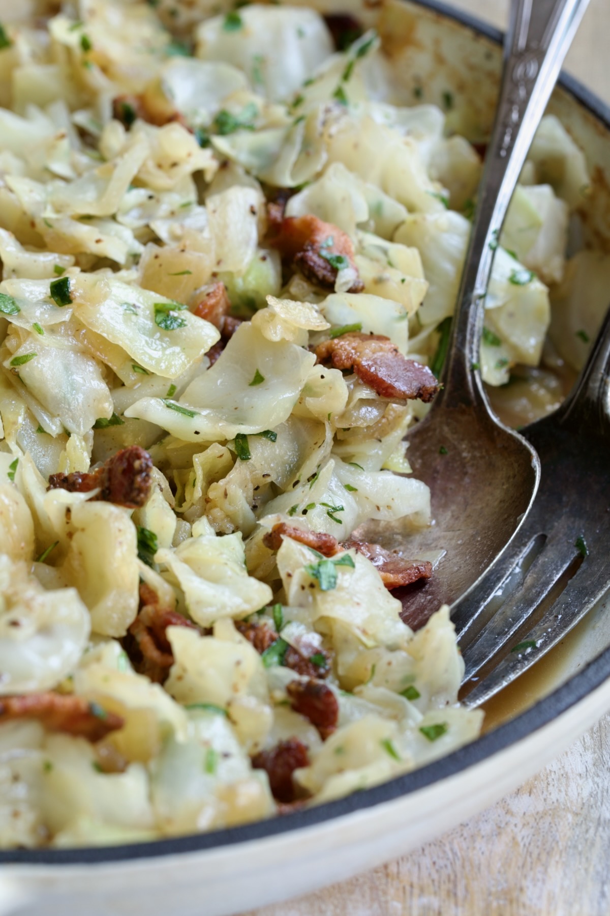 Two serving utensils serving up Fried Cabbage with Bacon.