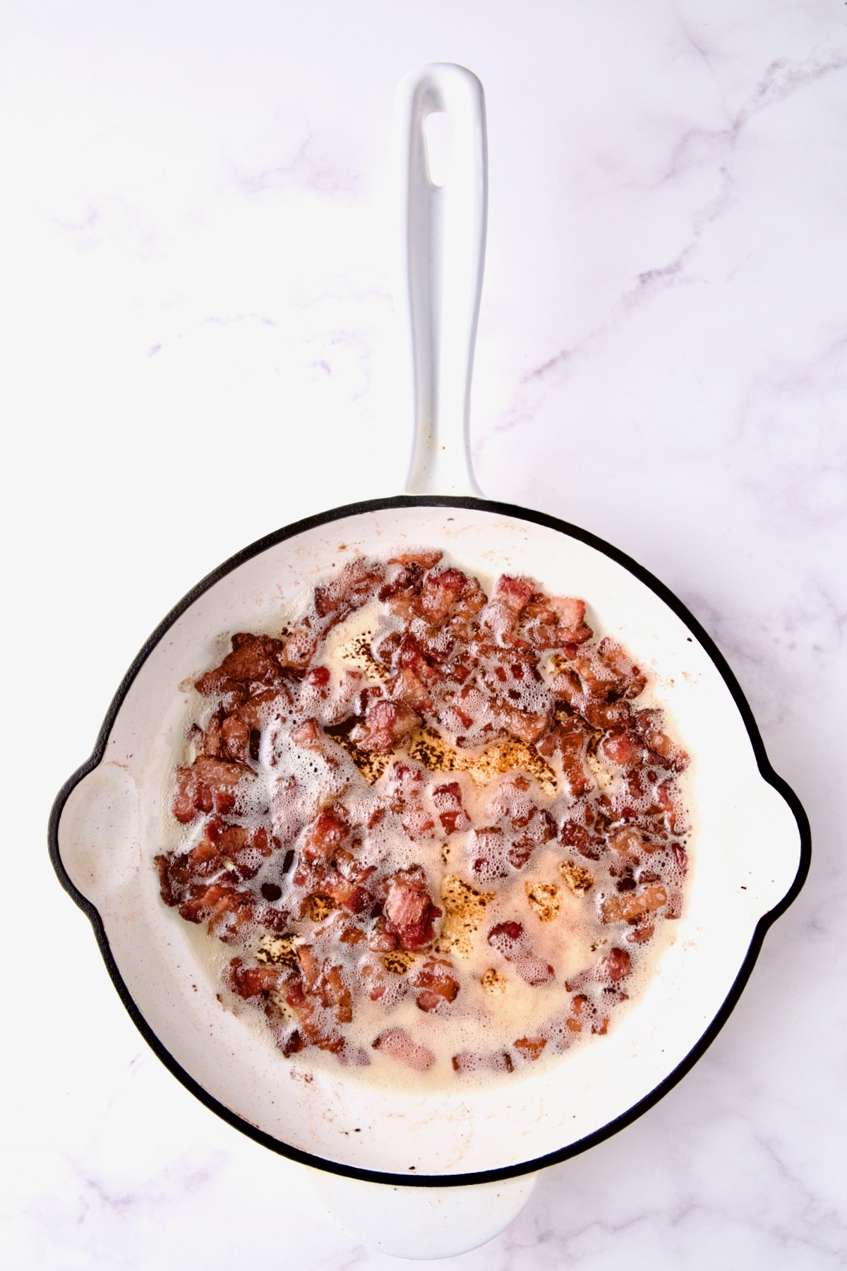 Cooked bacon in white enamel cast iron skillet.