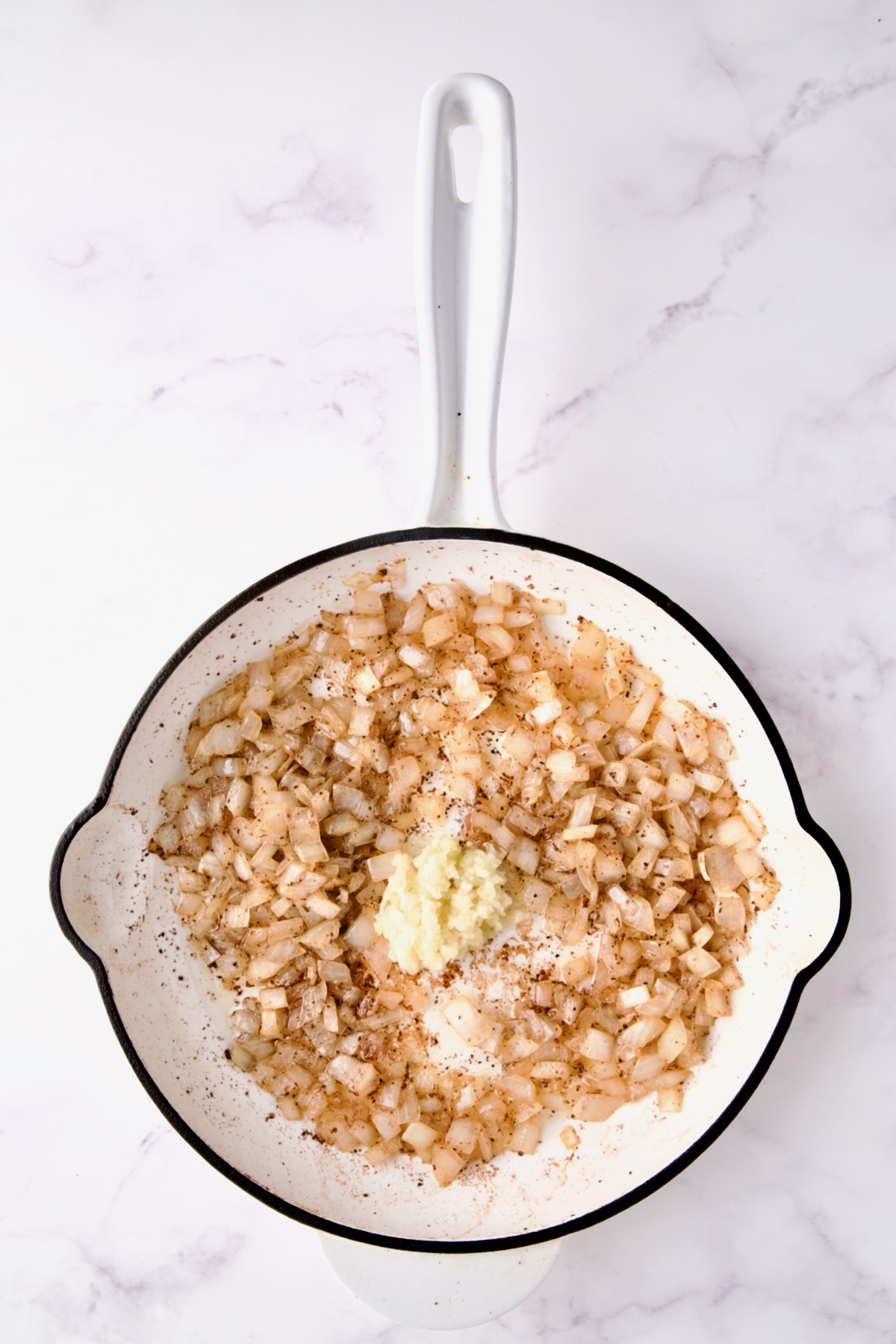 Cooked onions with fresh garlic added to white enamel cast iron skillet.