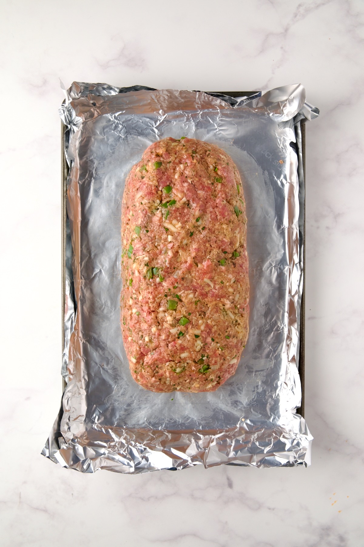 Meatloaf before being baked on aluminum foil-lined rimmed sheet pan.
