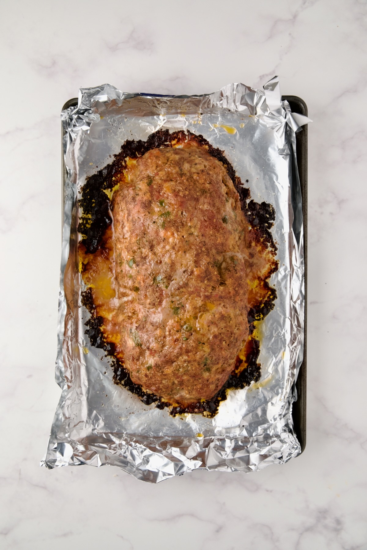 Baked meatloaf on aluminum foil-lined rimmed baking sheet.