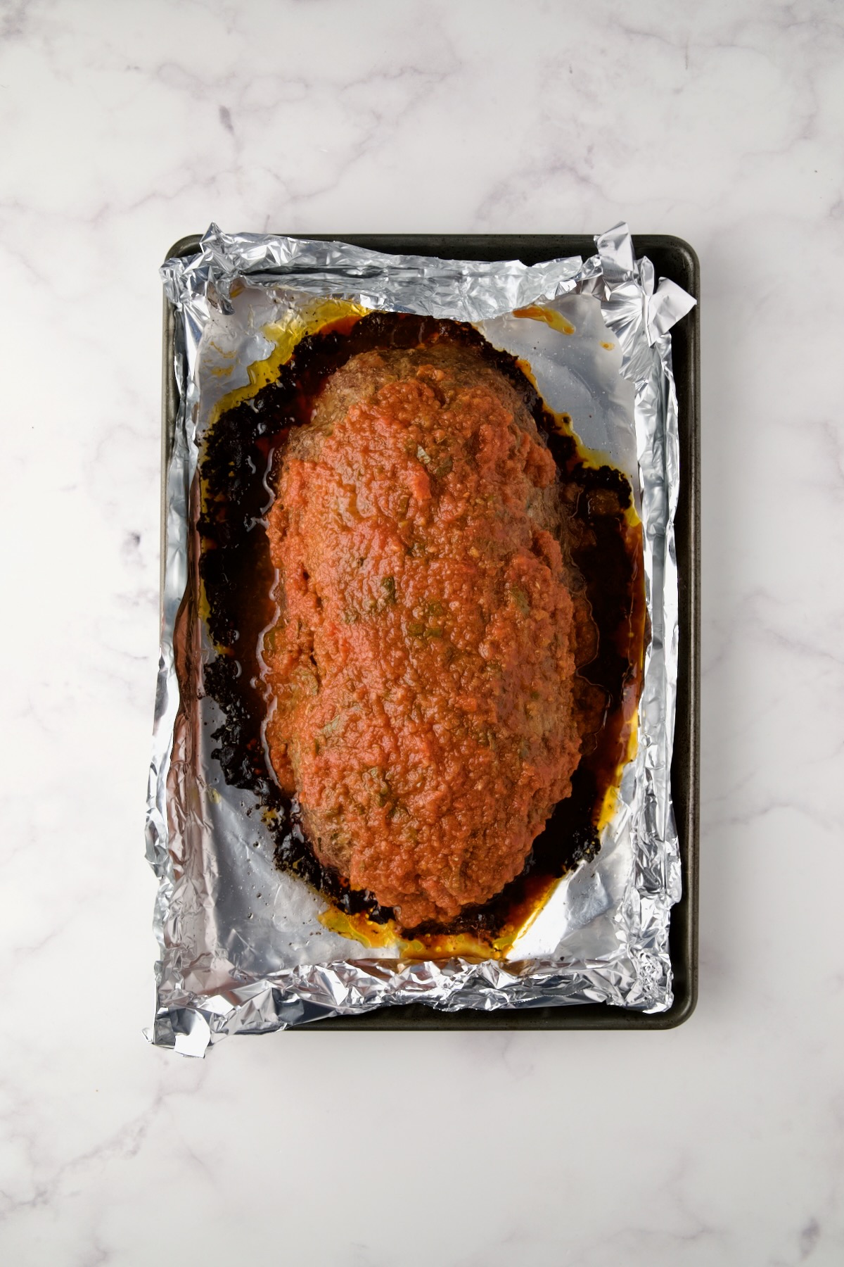 Baked meatloaf on aluminum foil-lined sheet pan with marinara sauce added.