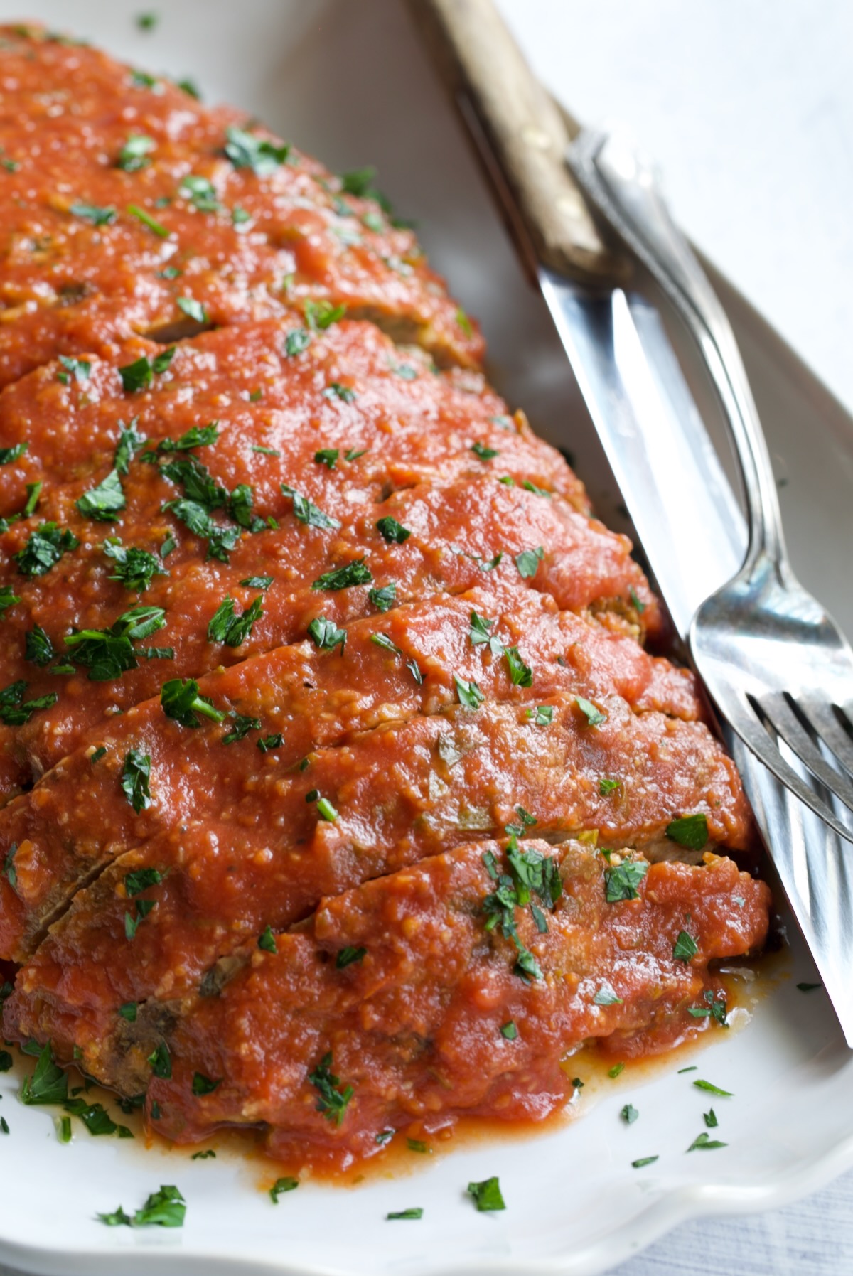 Italian Meatloaf on white platter garnished with chopped fresh parsley.