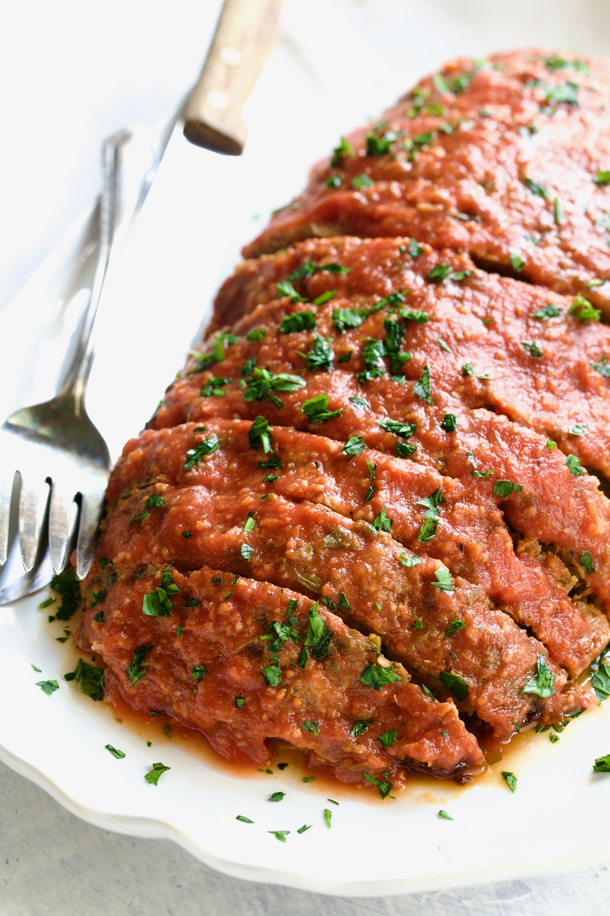 Italian Meatloaf on white platter with serving utensils.