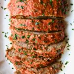 Italian Meatloaf on white platter with half of it sliced.