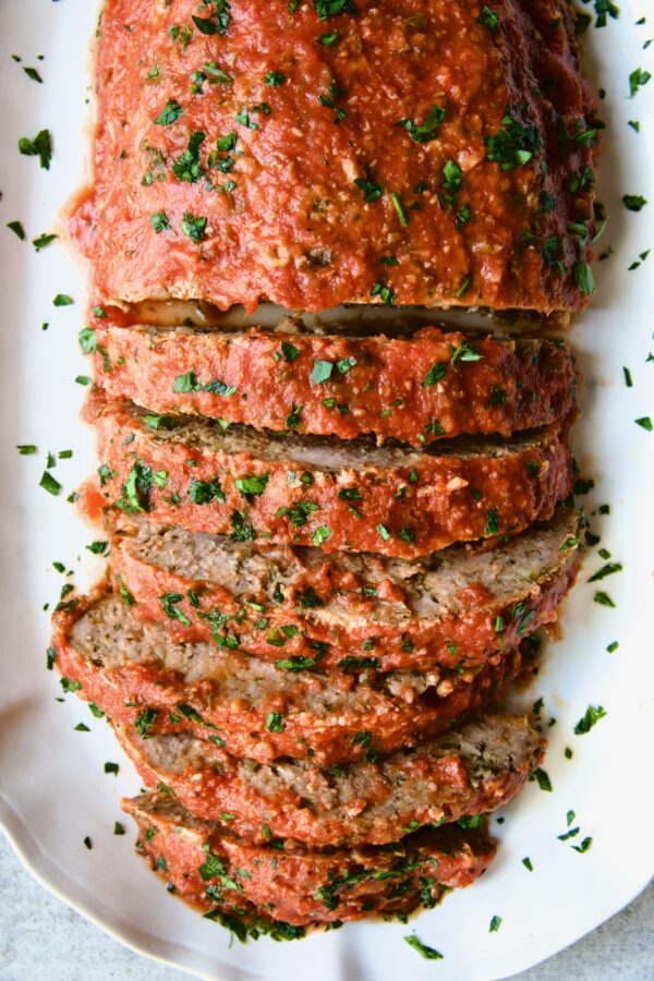 Italian Meatloaf on white platter with half of it sliced.