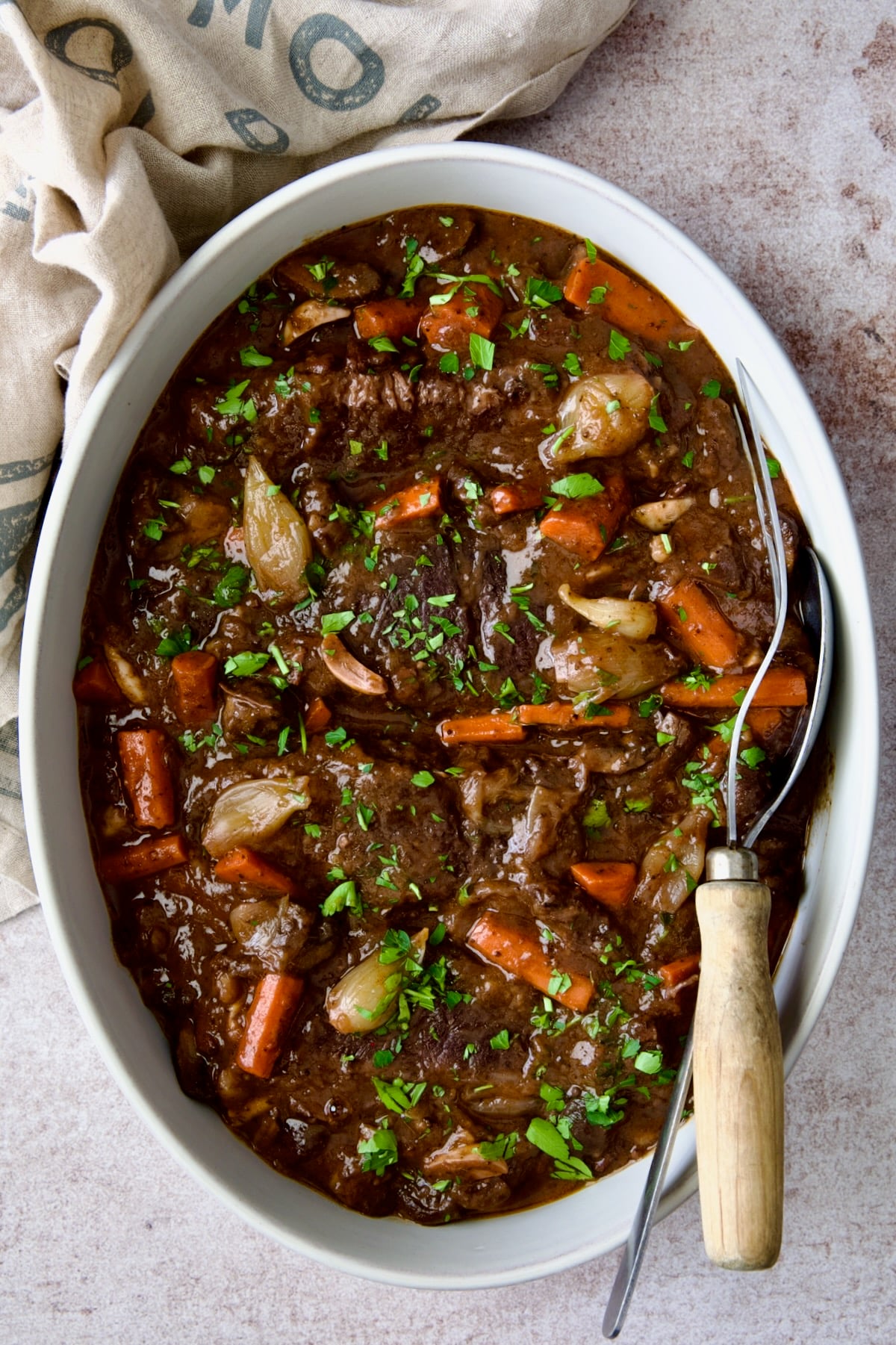 Short Ribs Bourguignon in white oval serving dish with meat fork and serving spoon.
