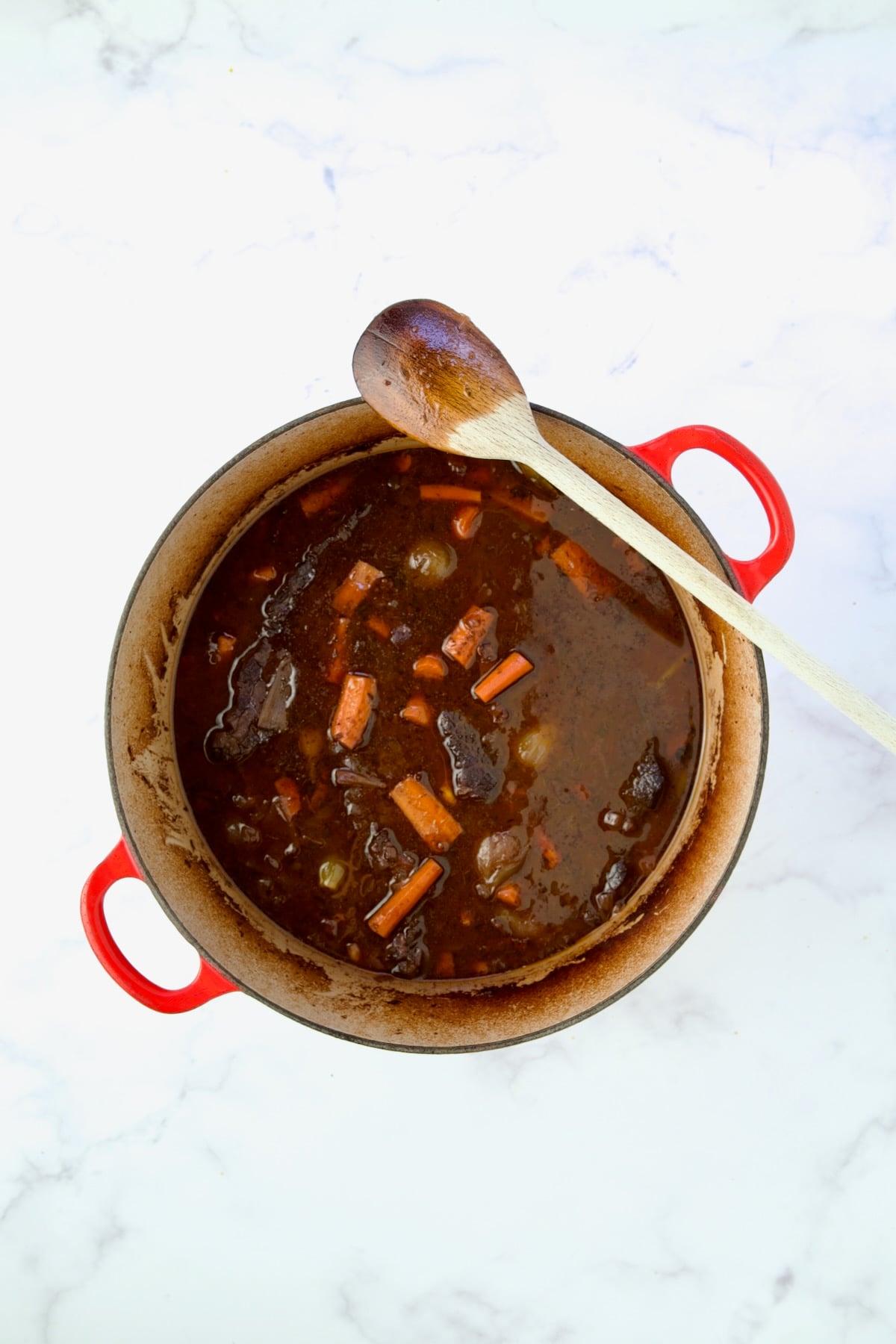 Recipe in red Dutch oven with wooden spoon before being thickened.